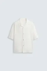 Camisa color crudo de corte holgado confeccionada en tejido texturizado tipo toalla. Tiene cuello bowling, manga corta, terminaciones irregulares y cierre frontal con botones a presión.