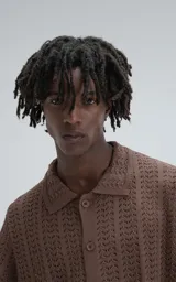 Camisa de tejido de punto color café, manga corta y cuello polo con botones frontales. Presenta un patrón calado de espiga o chevron.