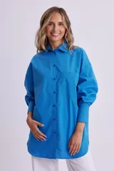 Camisa celeste de manga larga, corte oversize, con cuello clásico, cierre frontal con botones, bolsillo en el pecho y bajo redondeado.