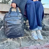 Mochila de eco-cuero color marrón, con múltiples bolsillos frontales y laterales, y asa superior.