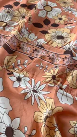 Maxivestido naranja con estampado floral en tonos amarillos, blancos y marrones, escote en V profundo, tirantes finos y cintura fruncida.