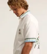 Camisa masculina de algodón con corte boxy, cuello con solapa y rayas, abotonado delantero, bolsillo con estampa floral y estampa trasera de palmera con la palabra 'Paradise'.