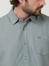 Camisa de manga corta color beige, con cuello clásico, cierre frontal con botones y bolsillo en el pecho izquierdo.