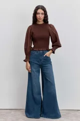 Blusa color marrón con cuerpo fruncido tipo nido de abeja, cuello alto con volados y mangas largas abullonadas con puños elásticos terminados en volados.