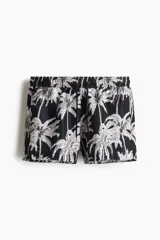 Short de baño negro con estampado de palmeras blancas, cintura elástica con cordón ajustable, bolsillos laterales y trasero.