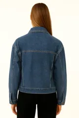 Campera de jean azul con cuello clásico, cierre frontal con botones dorados, bolsillos con solapa abotonada en el pecho y corte holgado.