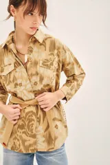 Campera de corte recto confeccionada en gabardina estampada con bordados de hilo. Presenta cuello camisero, cierre frontal con botones, dos bolsillos de parche con solapa en el pecho y lazo ajustable en la cintura con detalle bordado.