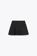 Falda pantalón corta de color negro, con tiro medio, detalle de pliegues en la cintura y volantes en el ruedo. Cierre lateral con cremallera.