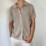 Camisa color beige de tejido calado, manga corta, cuello tipo polo y cierre frontal con botones.