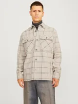 Sobrecamisa de manga larga color beige con estampado a cuadros en tonos grises y blancos. Tiene cierre con botones, cuello clásico y dos bolsillos con solapa abotonada en el pecho.