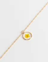 Cadena corta dorada con dije circular transparente que contiene una flor amarilla.