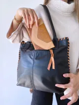 Bolso tipo tote de cuero negro con costuras a la vista en color camel. Tiene doble asa de hombro y está forrada en tela.