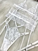 Conjunto de lencería blanco de encaje, compuesto por un corpiño triangular, una tanga de tiro alto con tiras dobles regulables, un portaligas con enganches desmontables y ligas regulables.