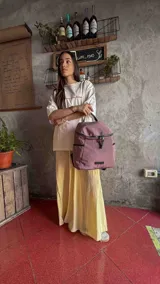 Mochila urbana de diseño compacto, color violeta/malva, con acabado ligeramente brillante. Presenta un compartimento principal con doble cierre superior y bolsillos laterales con cierre.