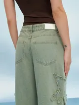 Pantalón de jean verde con corte acampanado y múltiples roturas con flecos.