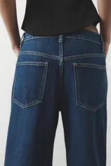 Pantalón de jean azul oscuro, de corte wide leg y tiro medio, con cinco bolsillos y cierre frontal con cremallera y botón metálico.