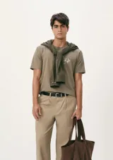 Camiseta blanca de algodón con cuello redondo y mangas cortas. Estampa rectangular con borde negro que contiene la frase "NATURAL ATMOSPHERE" en letras mayúsculas y una imagen de montañas y mar.