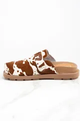 Zuecos con capellada de cuero con estampado animal print de vaca, base marrón con suela track y hebilla metálica ajustable.