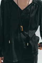 Blusa negra semitransparente con escote en pico, cordón ajustable y mangas largas con elástico en los puños.