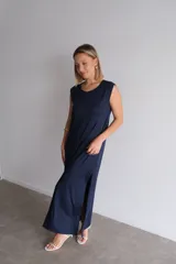 Vestido largo azul marino de tejido acanalado, con escote redondo y mangas cortas tipo hombrera. Presenta una abertura lateral en la falda.