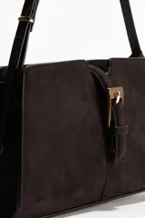 Cartera bandolera de hombro color marrón oscuro, con correa fina ajustable y cierre metálico dorado en la parte delantera. Incluye bolsillo interior con cierre y está forrada.