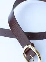 Cinturón marrón con textura símil cuero de cocodrilo y hebilla ovalada dorada.