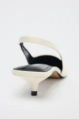 Zapato destalonado color crema con tacón fino y adorno en la parte delantera.