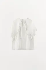 Top blanco de algodón con cuello redondo y manga corta con volados de encaje. Presenta bordados en el frente y cierre con botón en la espalda.