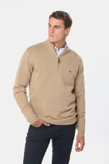 Buzo tejido de lana color beige, con medio cierre metálico y cuello alto. Tiene un pequeño logo bordado en el pecho.
