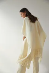 Ruana color crema de lana fina con flecos en el ruedo y bolsillos delanteros.