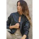 Camisa negra de cuero ovino con cuello mao, cierre frontal con botones a presión, dos bolsillos de parche en el pecho y tachas doradas en cuello, bolsillos y puños.