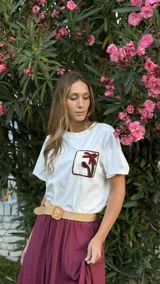 Remera blanca de corte boxy, con cuello redondo y manga corta. Presenta un bolsillo en el pecho con detalle de crochet con forma de palmera.