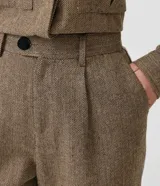 Pantalón de vestir de corte ancho, color marrón con textura tweed. Tiene cintura alta con trabillas, pliegues frontales, bolsillos laterales y un bolsillo trasero.