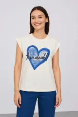 Remera color crudo de algodón con mangas cortas y cuello redondo. Estampado frontal con un corazón azul y texto en negro.