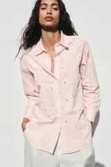 Camisa manga larga color rosa pálido con cuello solapa y cierre frontal con botones. Detalle de bordados perforados engomados con motivos florales. Corte recto.