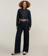 Camisa cropped de jeans azul oscuro, con cuello inglés, mangas largas, bolsillo en el pecho, pespuntes contrastantes y cierre con botones.