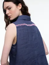 Camisa sin mangas negra de lino con cuello clásico, cierre frontal abotonado y bolsillo de parche en el pecho. Presenta bordados tipo pespunte en contraste en el frente y canesú trasero.