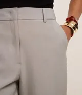 Pantalón de vestir gris claro, de corte recto, con bolsillos laterales y traseros. Se ajusta a la cintura con cinturón de cuero negro.