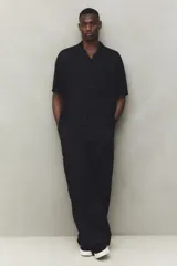 Pantalón cargo negro de corte holgado, con cintura elástica ajustable con cordón, bolsillos laterales al bies, bolsillos tipo cargo con solapa y botón a presión en las piernas y bolsillos traseros con solapa y botón a presión. Cuenta con pliegues cosidos en las rodillas y cordón ajustable oculto en el bajo.