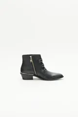 Bota corta de cuero negro con diseño inspirado en el estilo rocker. Presenta tres tiras frontales con remaches y hebillas metálicas color níquel, puntera metálica y taco ancho de 4 cm con detalle de vira metálica. Posee cierre lateral interno.