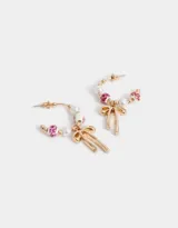 Aros tipo argolla dorados con cuentas de perlas, dijes de cerámica con estampado floral y dije de moño metálico.