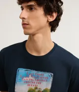 Remera azul marino de algodón, corte regular, cuello redondo y manga corta. Estampa rectangular con ilustración de barcos en la playa.