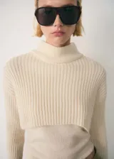 Sweater corto color crema de punto canalé con cuello alto.
