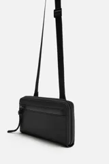 Bandolera negra con acabado engomado, compartimento principal con cierre de cremallera y bolsillo interior con cremallera. Asa de hombro ajustable y extraíble.