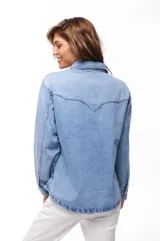 Sobrecamisa celeste de jean con cuello camisero, cierre frontal con botones dorados, dos bolsillos con solapa en el pecho y mangas largas con puños abotonados.
