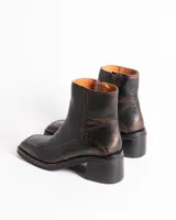 Bota corta de cuero charol negro, con caña baja, cierre lateral y taco cuadrado de madera.