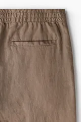 Pantalón marrón claro de lino, corte recto, con cintura elástica y cordón ajustable. Posee bolsillos laterales y trasero.