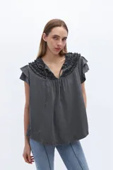 Remera gris con escote en V y volados en el cuello y mangas cortas.