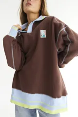 Buzo celeste con cuello polo y puños en rib color verde lima. Tiene un parche con el logo de la marca en el pecho y rayas horizontales en el ruedo.