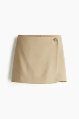 Short pollera color beige, de corte mini y diseño cruzado con botón decorativo.